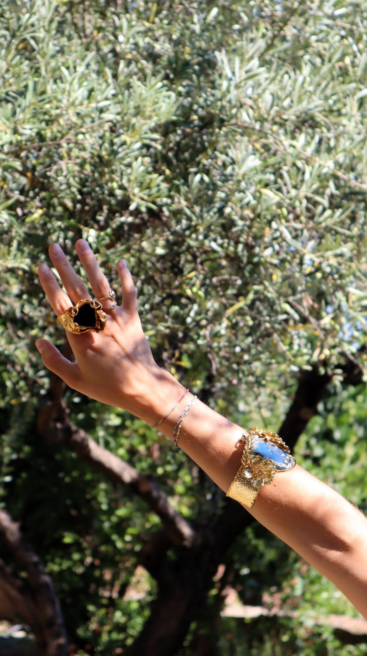 Hand with gold ring and bracelet against a blurred natural background